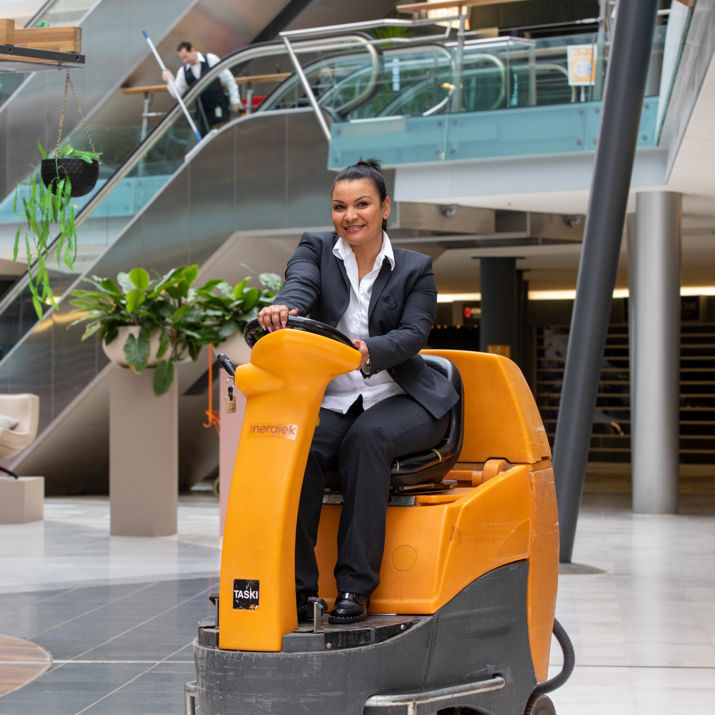 Schoonmaakmedewerker die de vloer aan het schoonmaken is op een schrobmachine