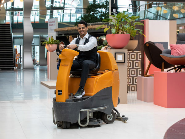 Schoonmaakmedewerker die vloeren aan het schoonmaken is op een schrobmachine