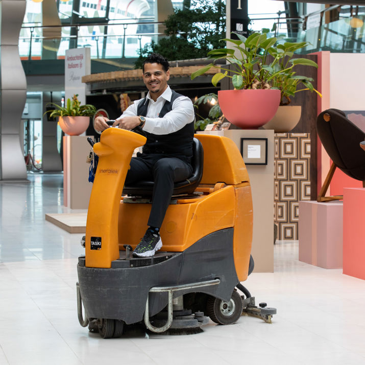 Schoonmaakmedewerker die vloeren aan het schoonmaken is op een schrobmachine