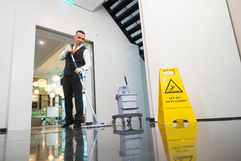 Schoonmaakmedewerker die de vloer aan het dweilen is