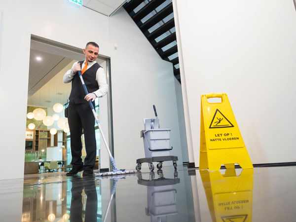 Schoonmaakmedewerker die de vloer aan het dweilen is