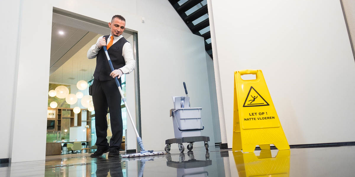 Schoonmaakmedewerker die de vloer aan het dweilen is