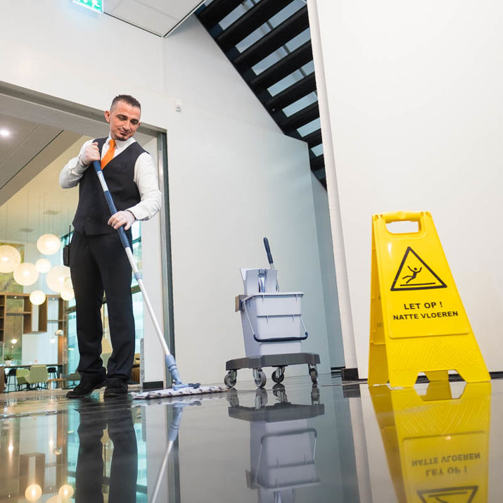 Schoonmaakmedewerker die de vloer aan het dweilen is