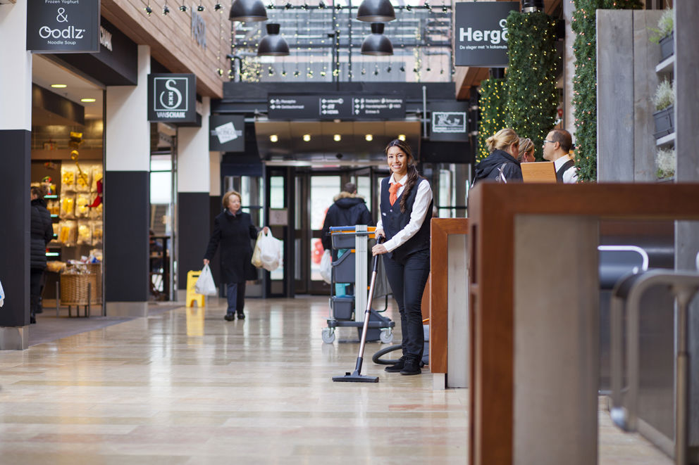 Schoonmaakmedewerker die de vloer aan het stofzuigen is in een winkelcentrum