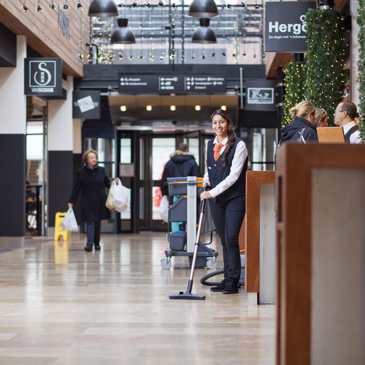 Schoonmaakmedewerker die de vloer aan het stofzuigen is in een winkelcentrum