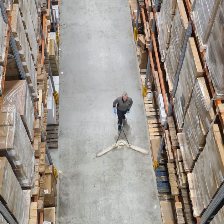 Schoonmaakmedewerker die een vloer aan het vegen is in een magazijn